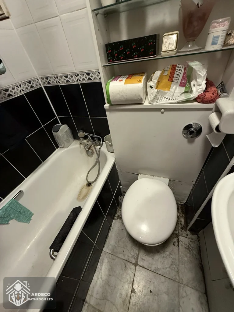 Bathroom before renovation in St John's Wood, showing old bath, toilet, black wall tiles and existing storage