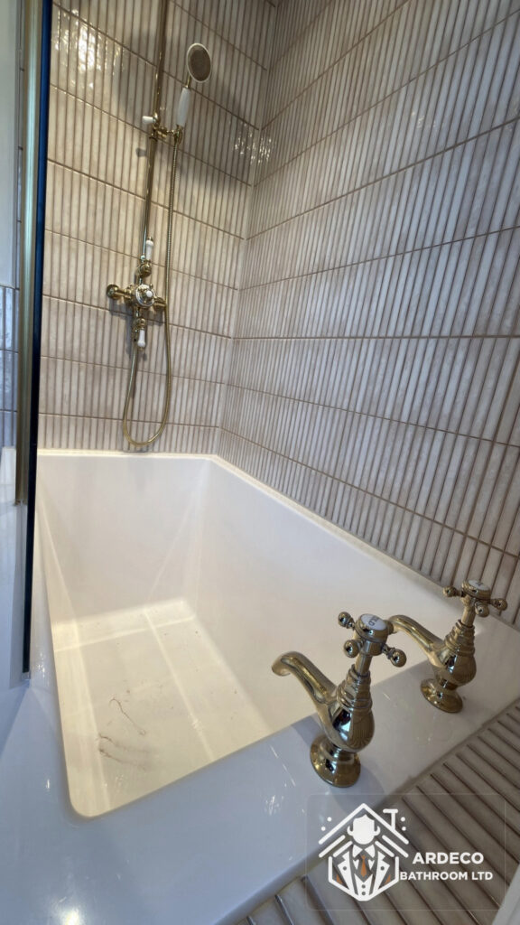 After renovation – bath with brass taps New bath with brass taps and shower fittings against vertically laid wall tiles